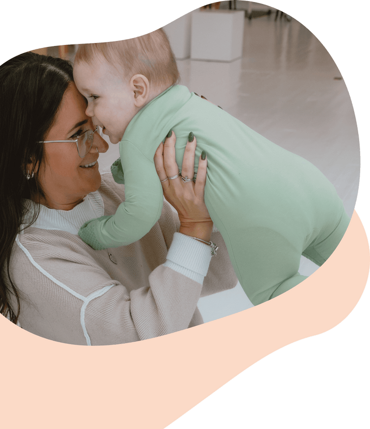 Mom cuddling with a baby in a green Scoot Suit